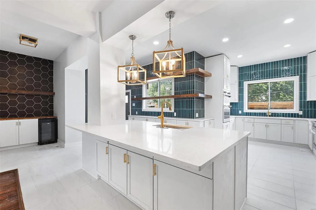 A white kitchen with quartz countertops and gold chandeliers.